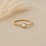 Gold ring with a small opal stone on a beige background