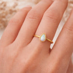 Gold ring with a teardrop-shaped opal stone on a hand