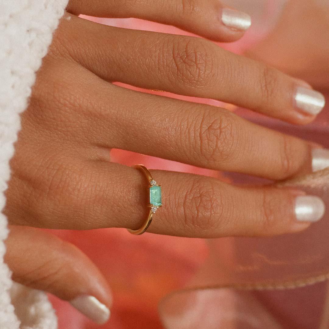 Hand wearing a dainty gold plated sterling silver tourmaline ring with a rectangular blue green centre stone, round cubic zirconia side accents, and a slim stackable band