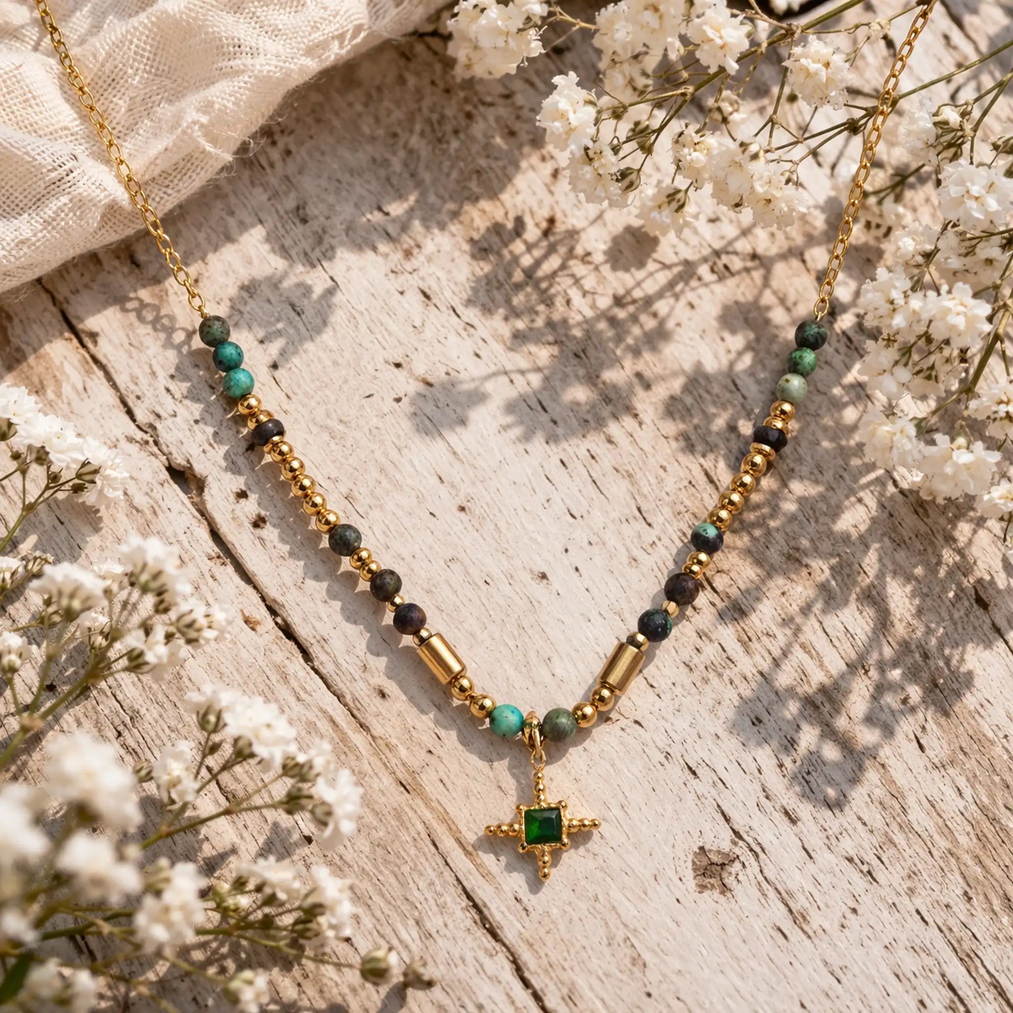 Gold necklace with green beads and a star pendant on a wooden surface with white flowers.