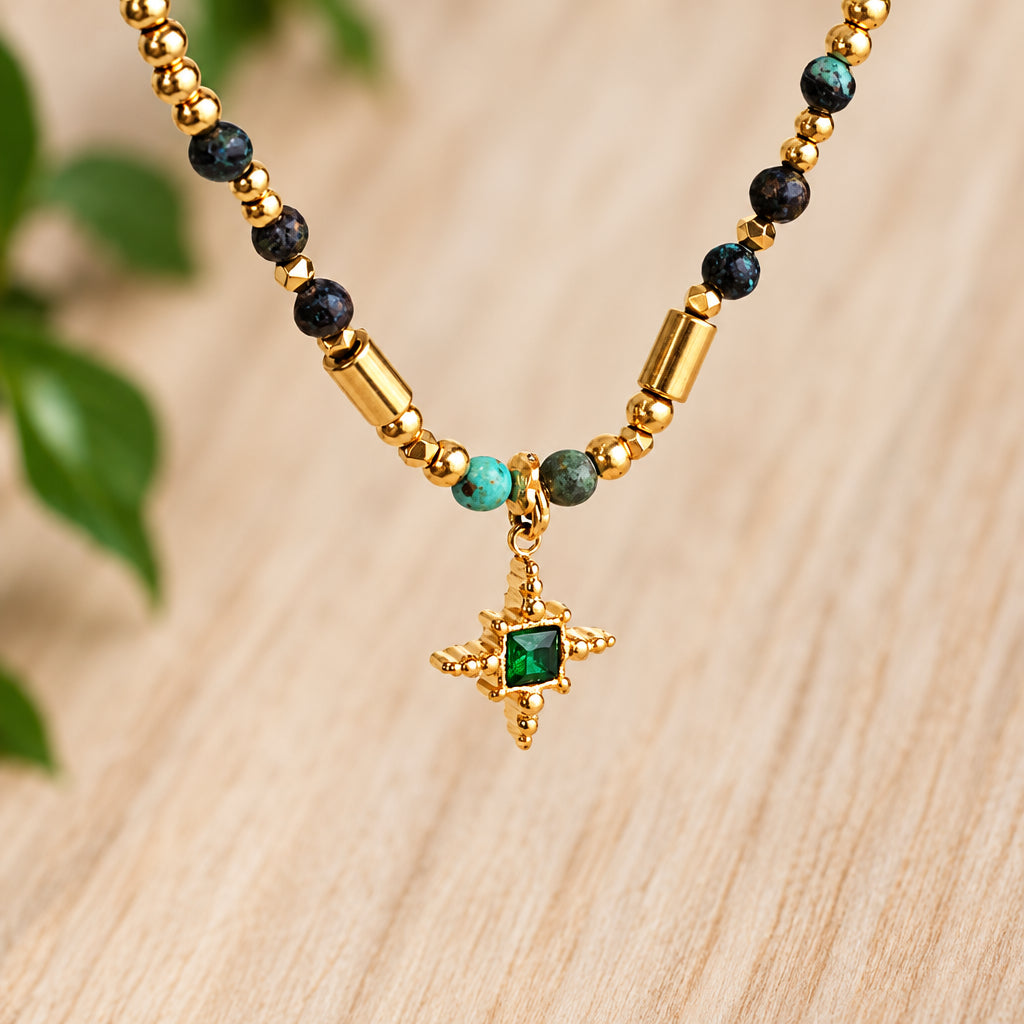 Turquoise beaded necklace with a green starlight cross pendant over a light wood surface