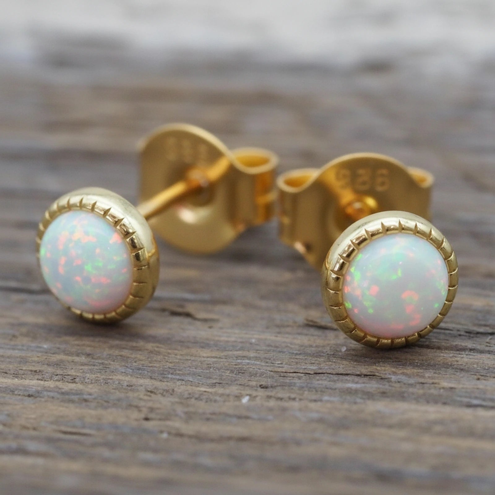 Gold White Opal stud earrings on a wood background
