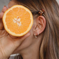 Small gold pavé huggie hoop earrings with cubic zirconia worn on a耳, shown next to an orange slice.