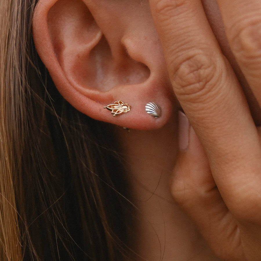 woman wearing one gold lotus stud earring and one sterling silver sea shell stud earring