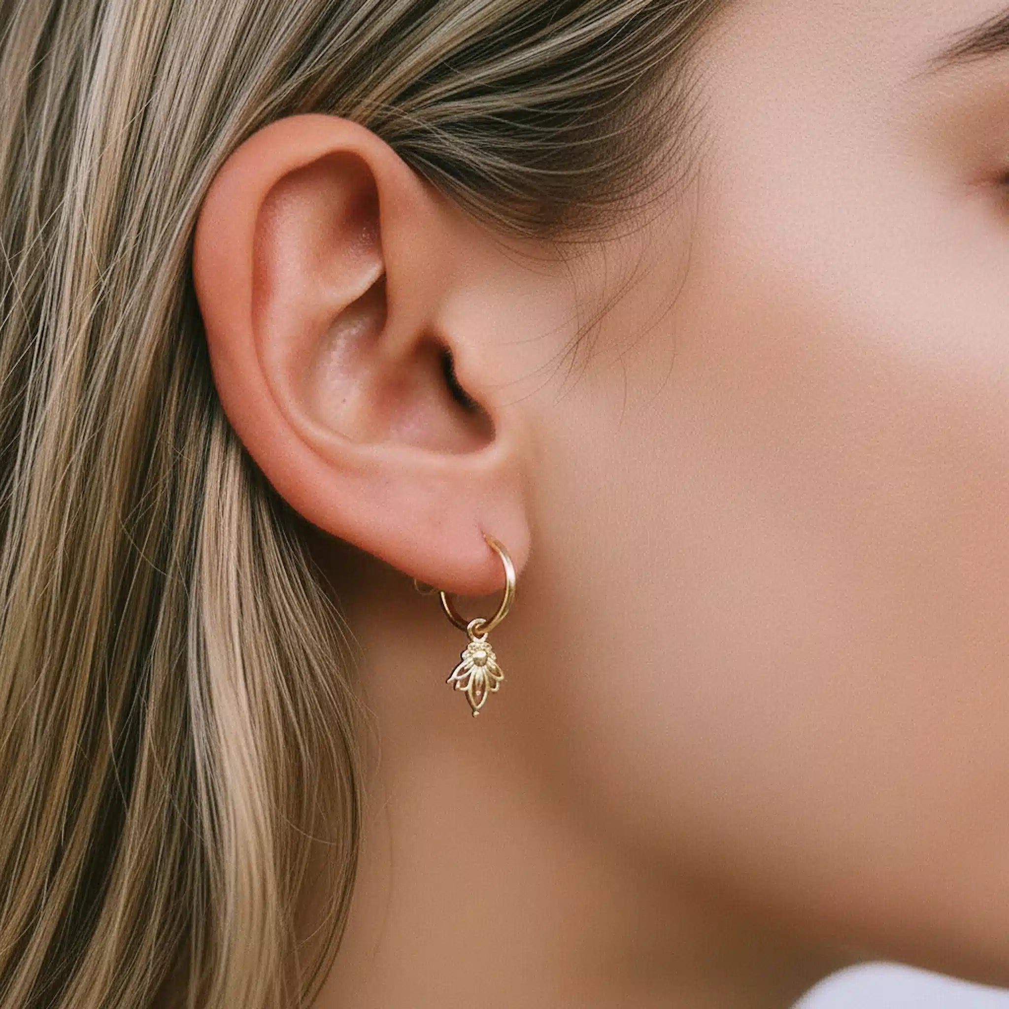 Close-up of a person wearing a gold hoop earring with a lotus flower charm pendant.