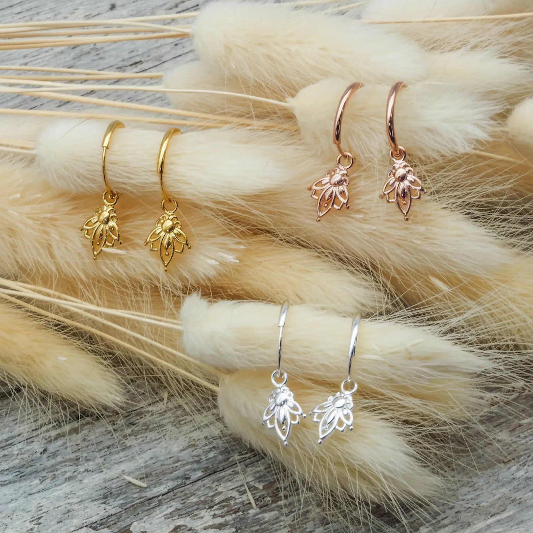 Gold, rose gold and silver lotus hoop earrings on dried flowers with a neutral background
