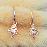 Pair of rose gold hoop earrings with lotus flower charms on a fluffy beige background