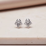 Pair of silver lotus flower stud earrings on a beige surface