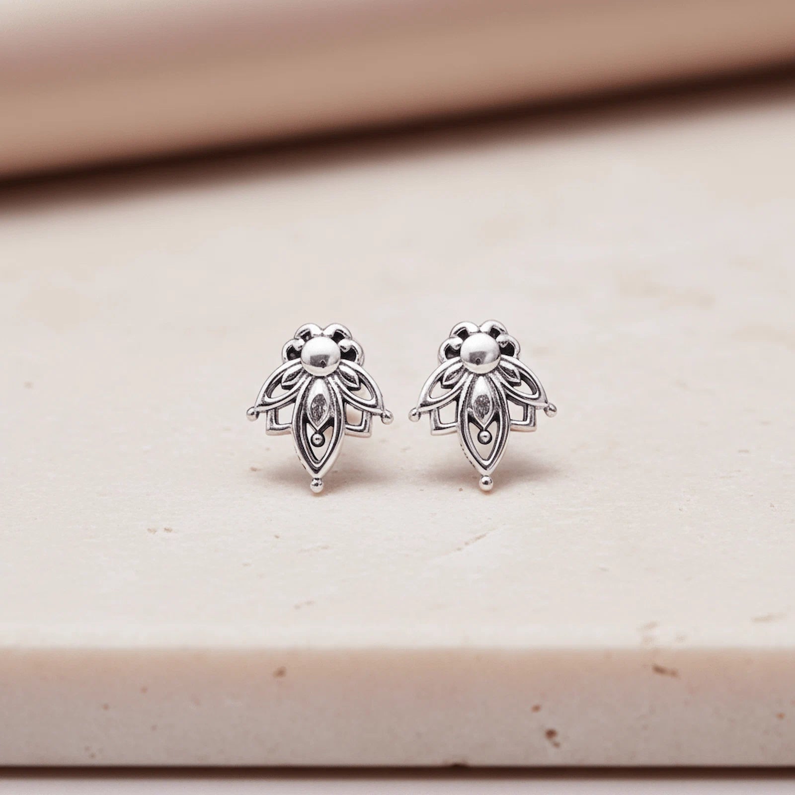 Pair of silver lotus flower stud earrings on a beige surface