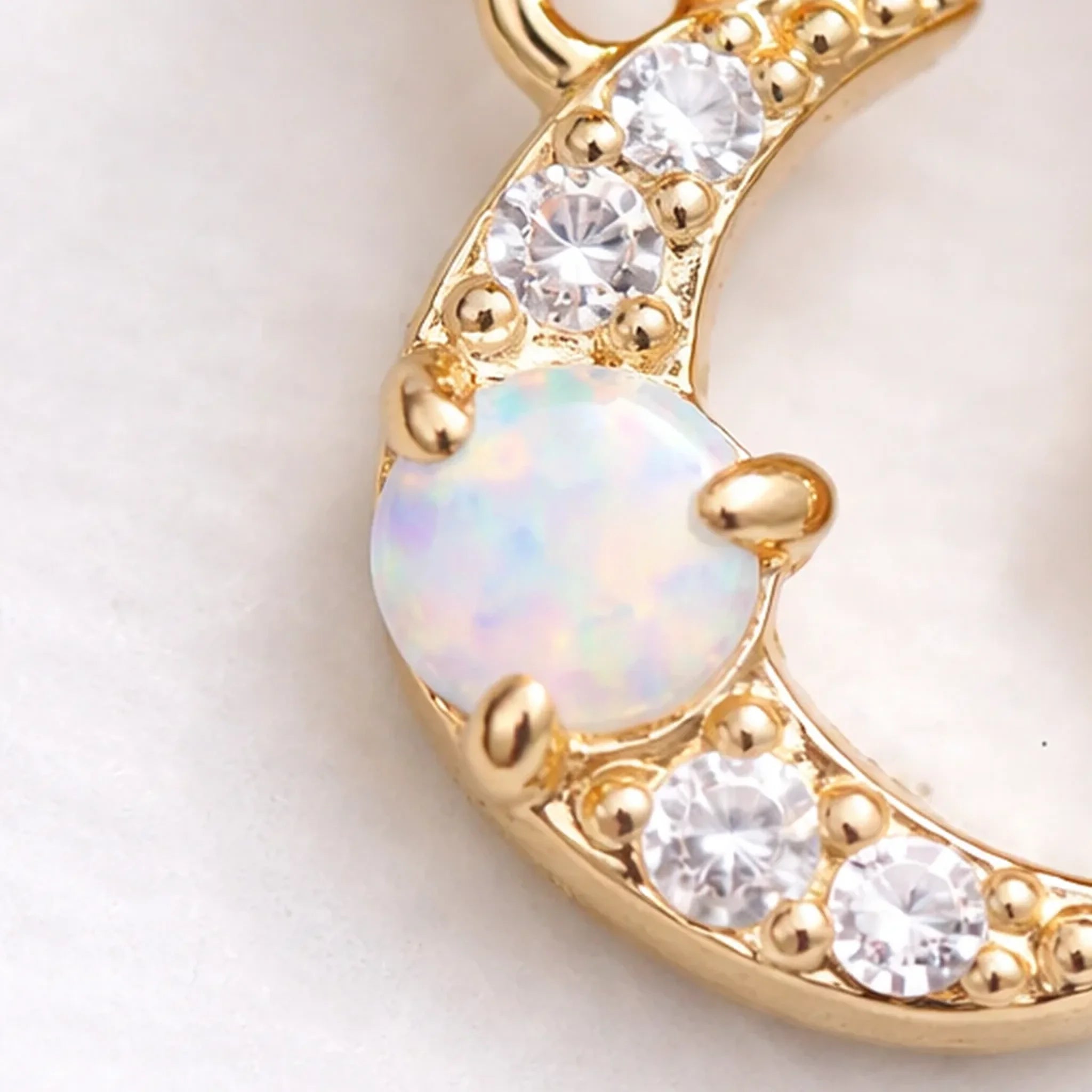 Gold pendant with opal and clear cubic zirconias gemstones on a light background