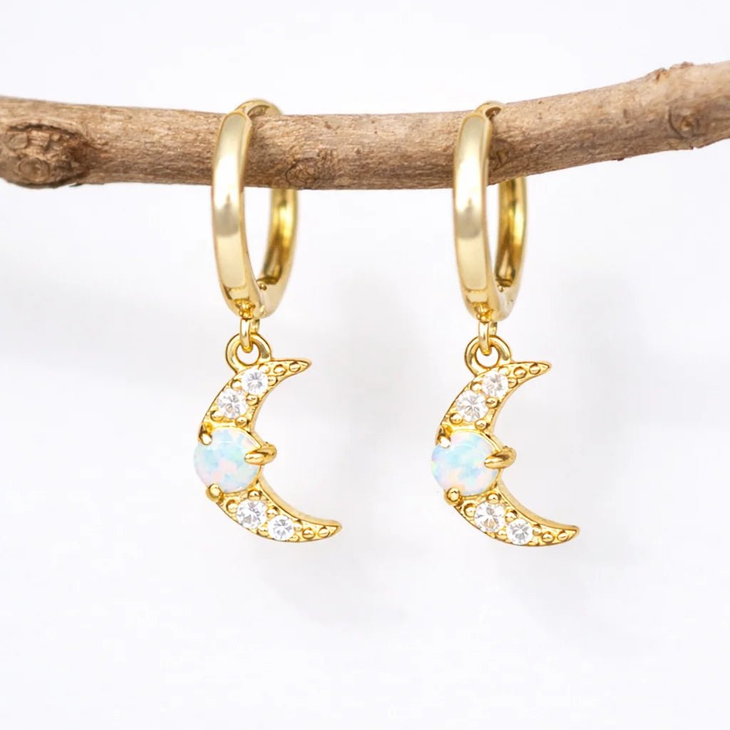 Gold hoop earrings with moon designs hanging on a branch against a white background