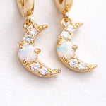 Gold moon-shaped earrings with opal stones on a light background