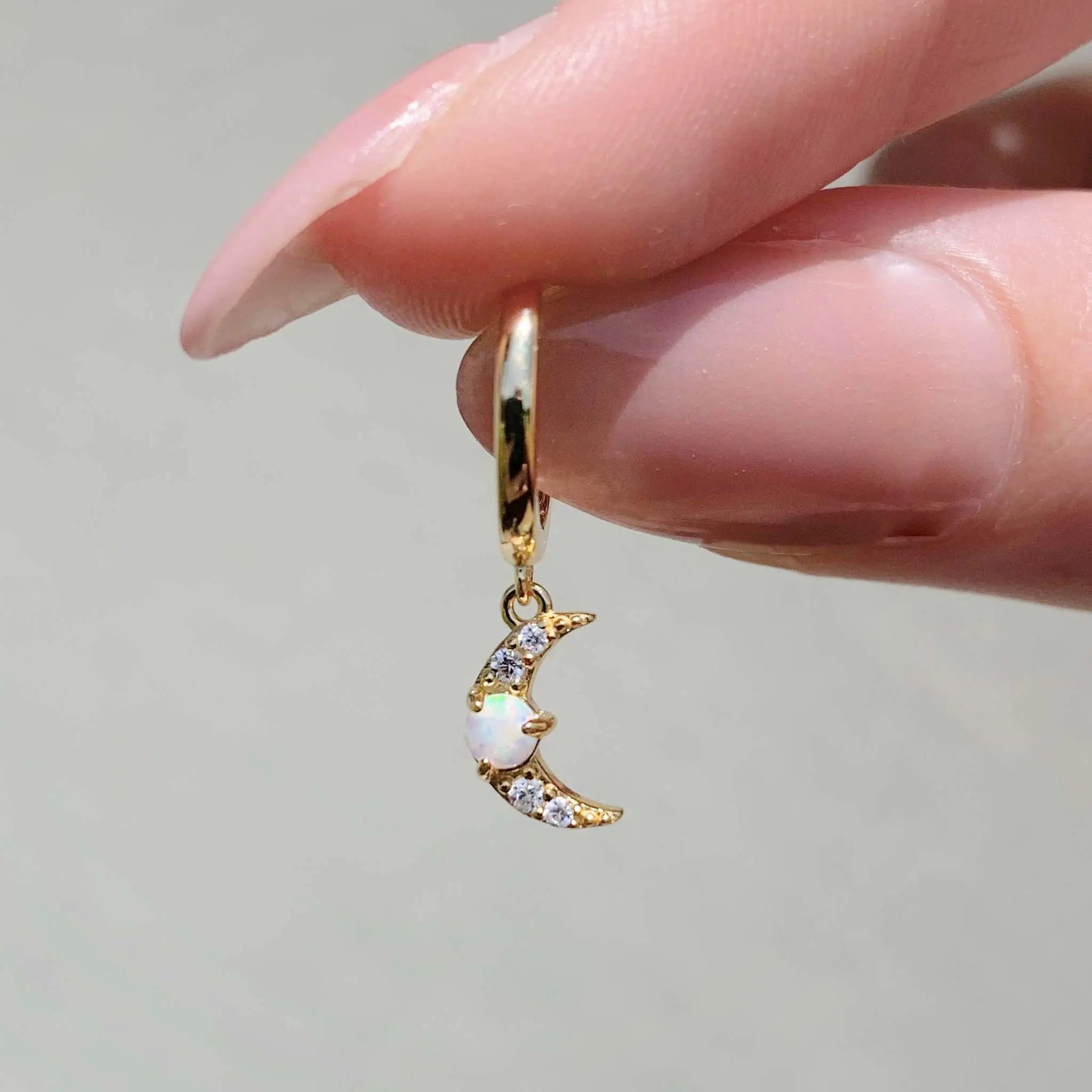 Gold hoop earring with a moon and opal design held between fingers against a neutral background