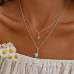 Close-up of a person wearing two sterling silver necklaces with natural rainbow moonstone pendants