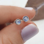 Silver earrings with moonstone gemstones held between fingers against a neutral background