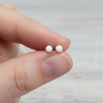 Opal stud earrings held between fingers against a neutral background