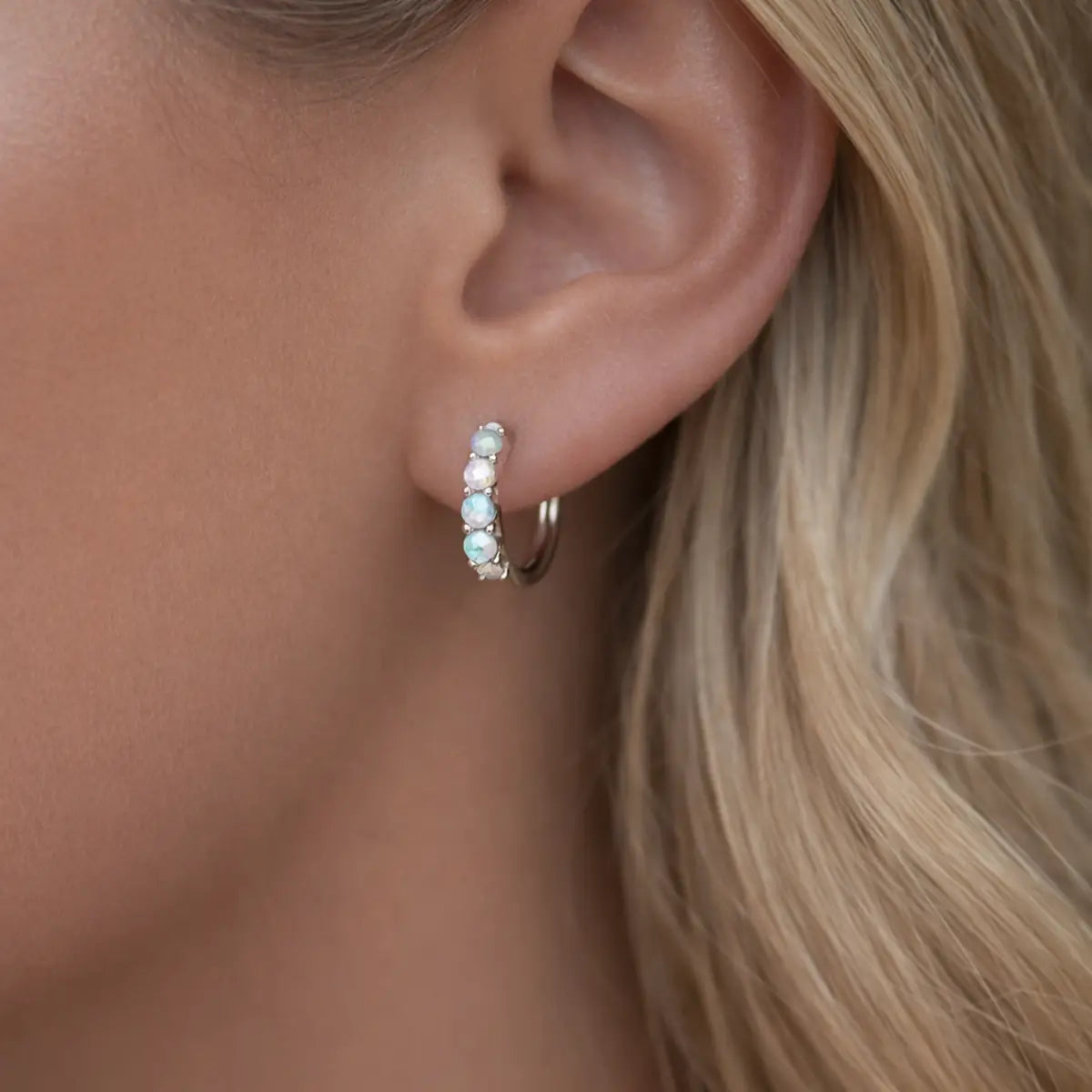 Close-up of an ear wearing a silver hoop earring with small opal gemstones.