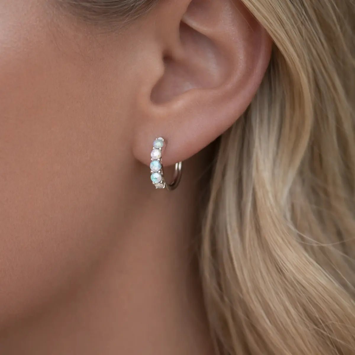 Close-up of an ear wearing a silver hoop earring with small opal gemstones.