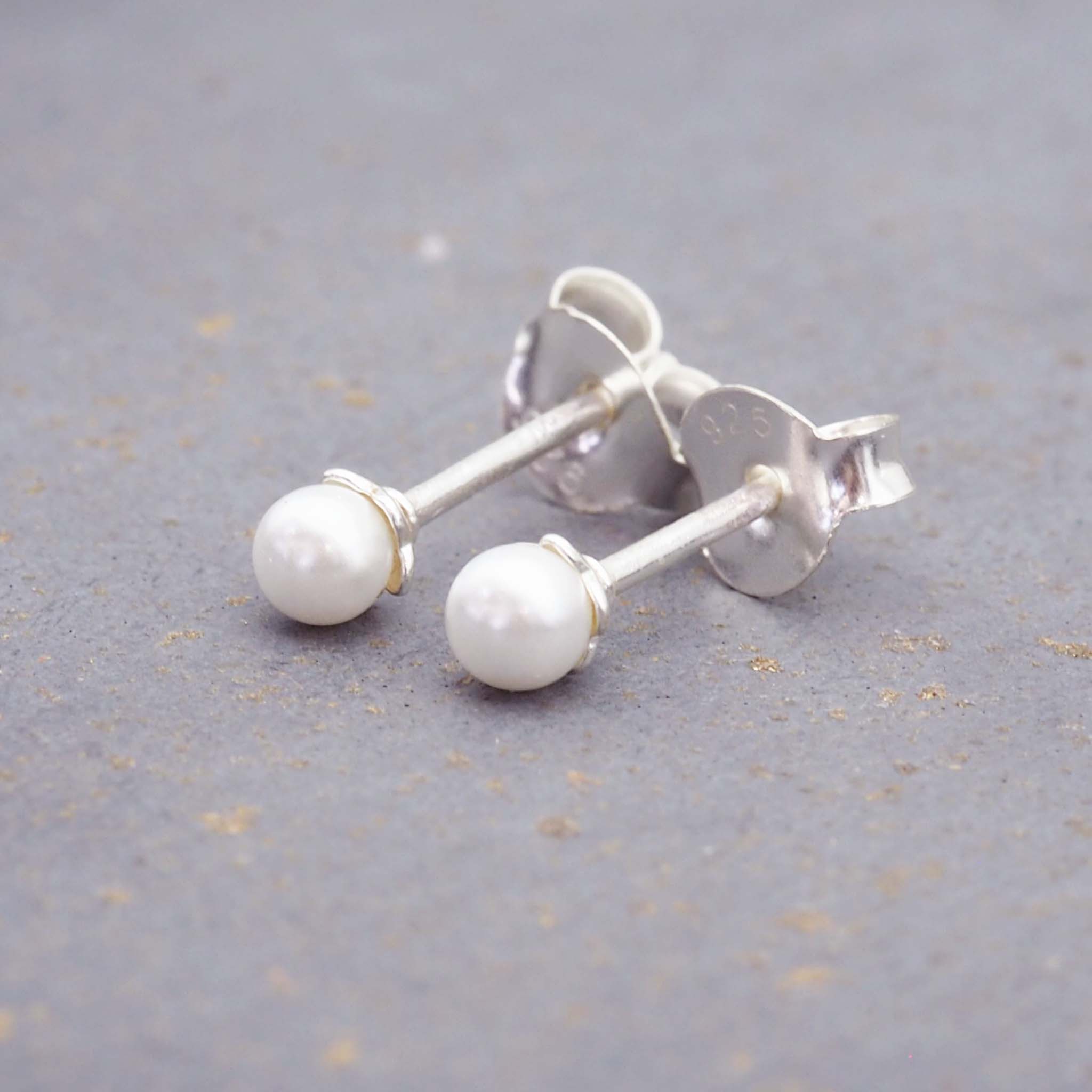 dainty sterling silver pearl stud earrings on a grey surface