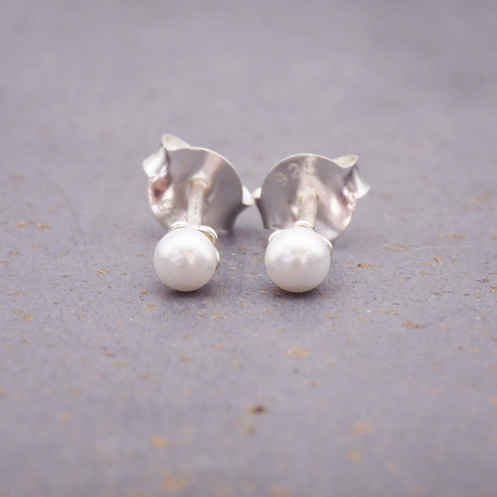 dainty sterling silver pearl stud earrings on a grey surface