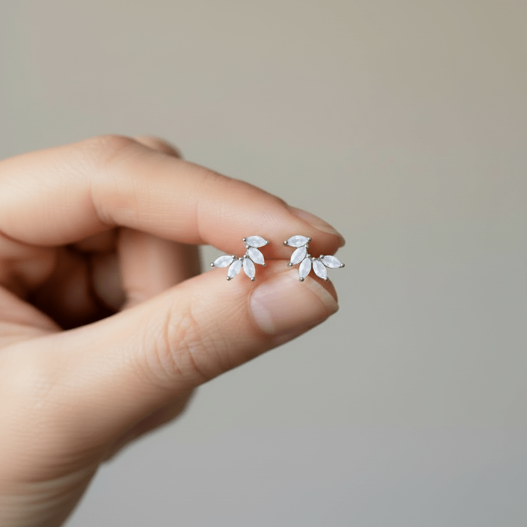 Hand holding a pair of silver leaf-shaped earrings against a neutral background