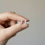 Hand holding a pair of silver leaf-shaped earrings against a neutral background