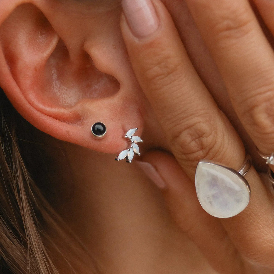 Woman wearing onyx stud earrings and petal shaped earrings.