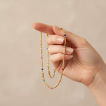 Hand holding a beaded necklace with multicolored beads against a beige background