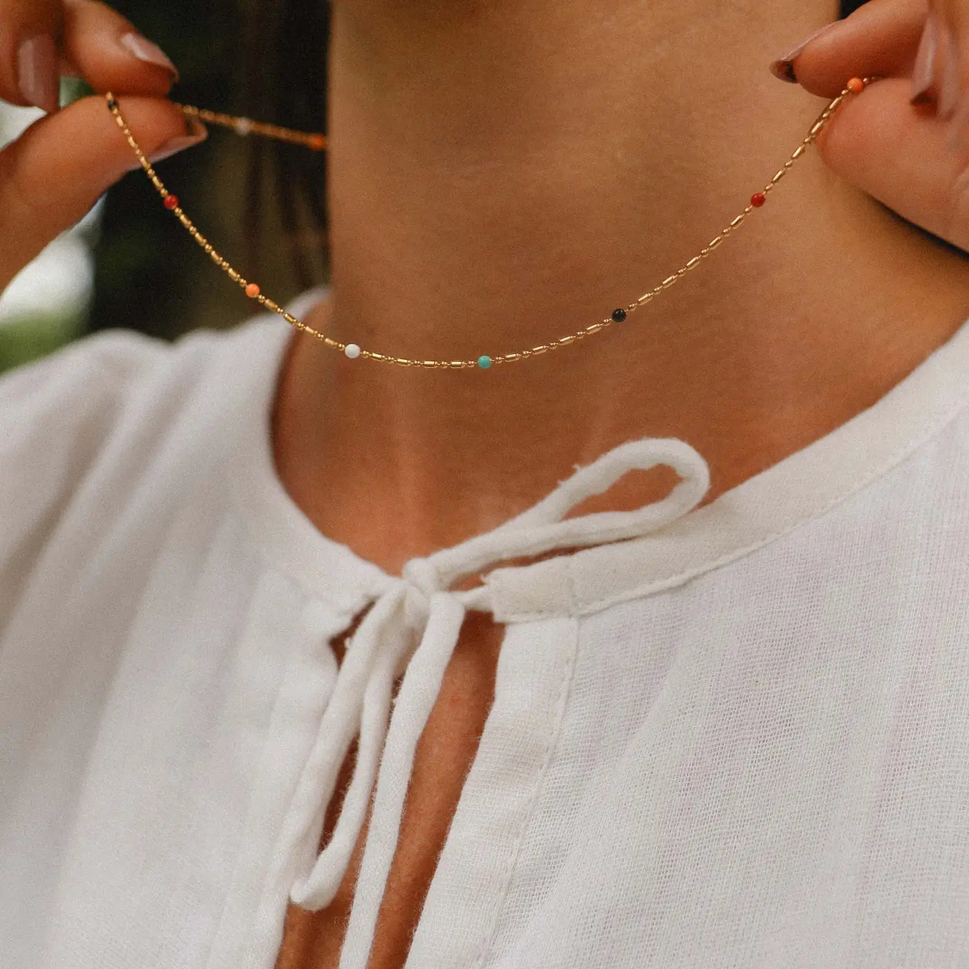 Woman wearing a delicate gold rainbow beaded necklace, dainty colourful seed beads, minimalist boho jewellery style.