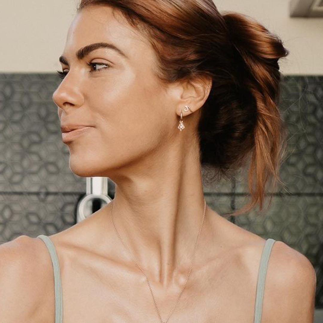 Woman with a ponytail wearing earrings and a necklace against a tiled wall background