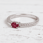 Silver ring with a ruby on a wooden surface with red rose petals.
