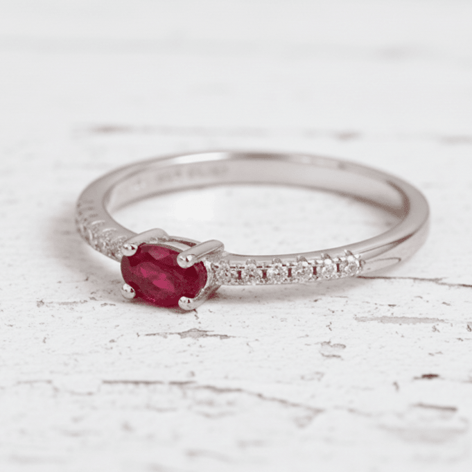 Silver ring with a ruby on a wooden surface with red rose petals.