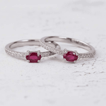 Two silver rings with red ruby gemstones on a white surface with pink petals.