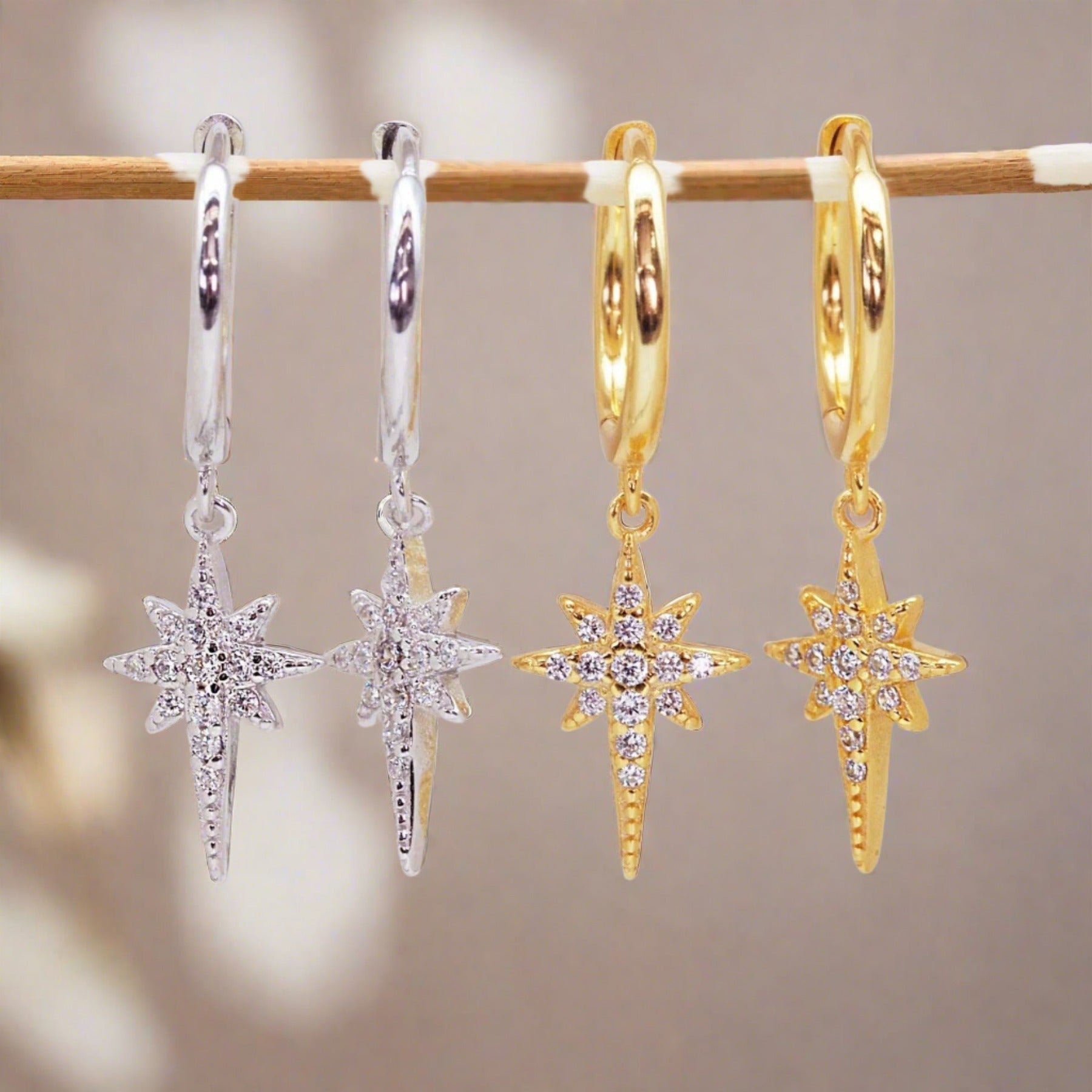 Pair of sterling silver and gold star-shaped earrings with cubic zirconias on a stick against a blurred background
