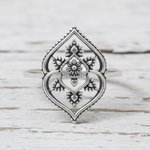 Silver ring with intricate design on a light wooden background