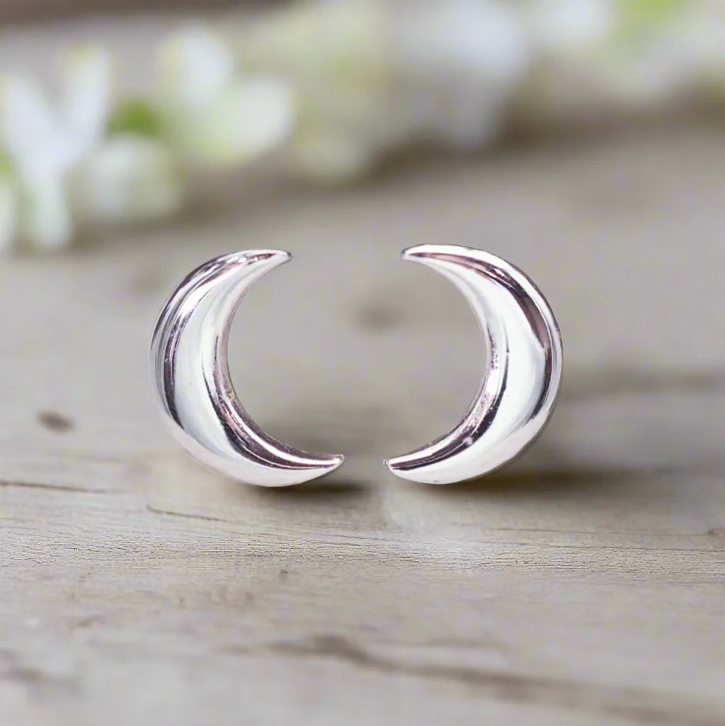 Silver crescent moon earrings on a wooden surface with a blurred floral background