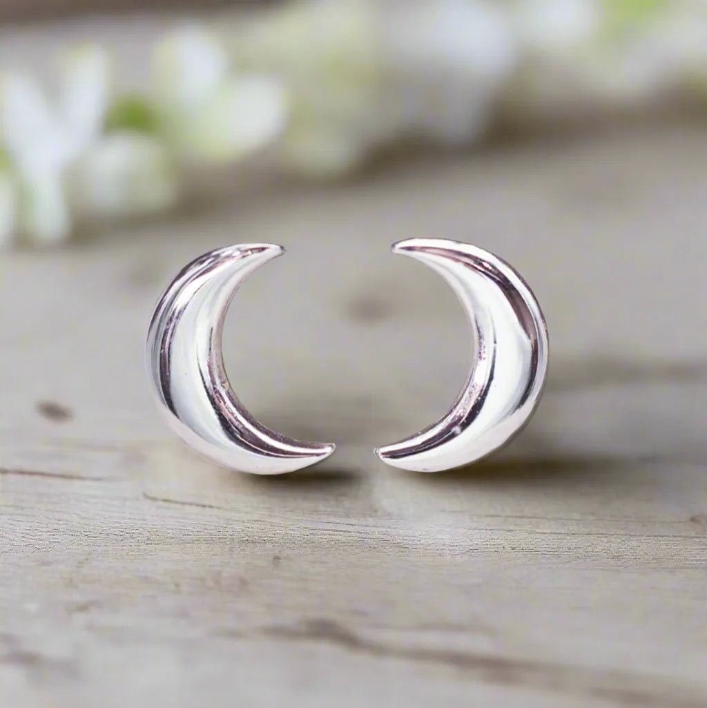 Silver crescent moon earrings on a wooden surface with a blurred floral background