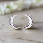 Silver crescent moon earrings on a wooden surface with a blurred floral background