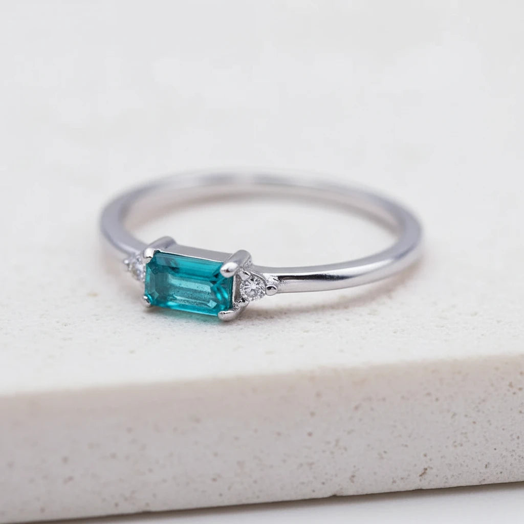 Dainty gold plated sterling silver gemstone ring with rectangular blue green tourmaline centre stone, round cubic zirconia side accents, and slim polished stackable band