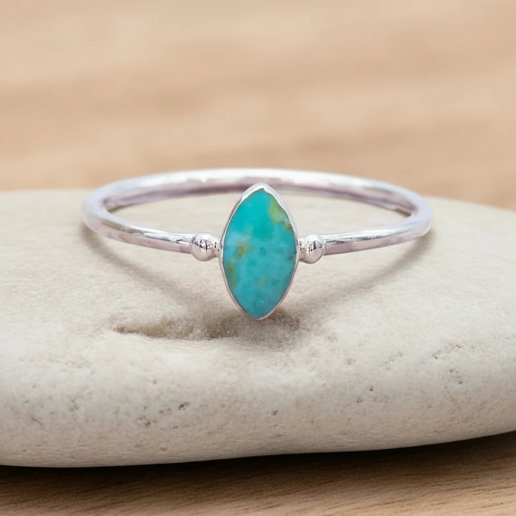Silver ring with a turquoise stone on a beige surface with dried grass in the background
