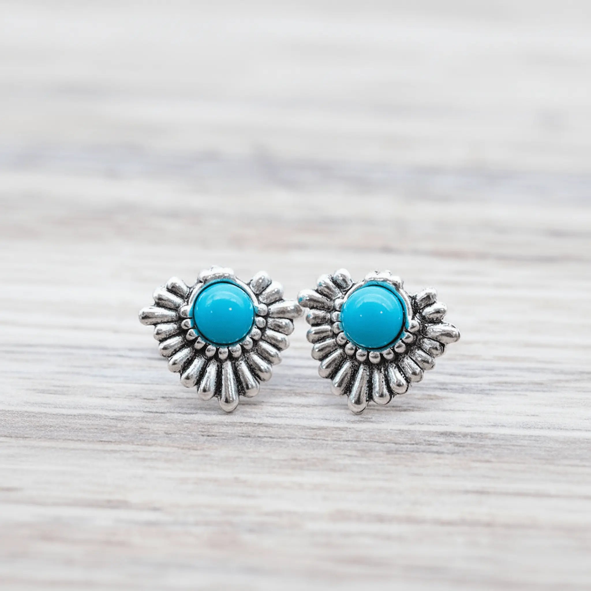 Pair of silver earrings with turquoise stones on a light wooden surface