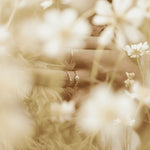 Hand wearing the gold snowflake ring with other gold rings in a field of white flowers