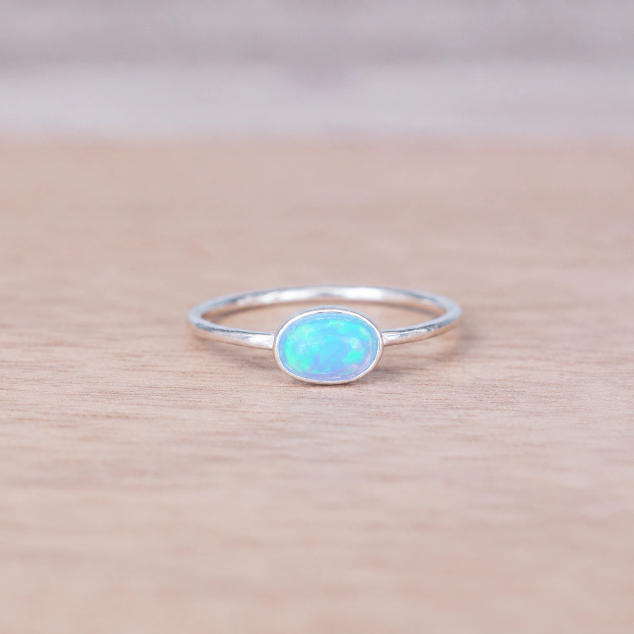 Silver blue opal ring with a cabochon, bezel-set oval lab-grown blue opal stone on a wooden surface