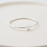 side shot of a dainty sterling silver heart ring on a light surface
