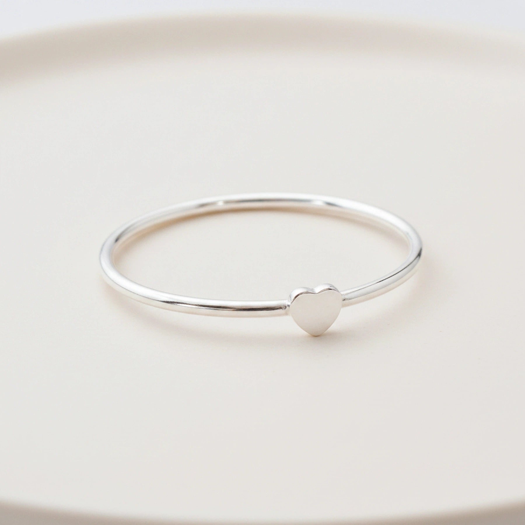 side shot of a dainty sterling silver heart ring on a light surface