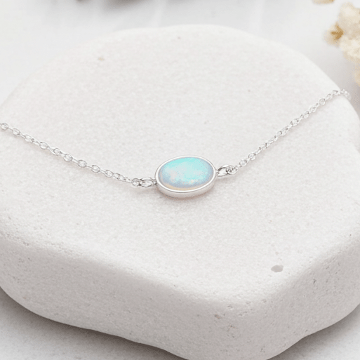 Silver bracelet with a white opal gemstone on a white stone surface with greenery