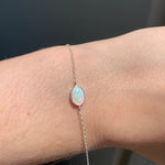 Silver bracelet with an opal stone on a wrist against a dark background