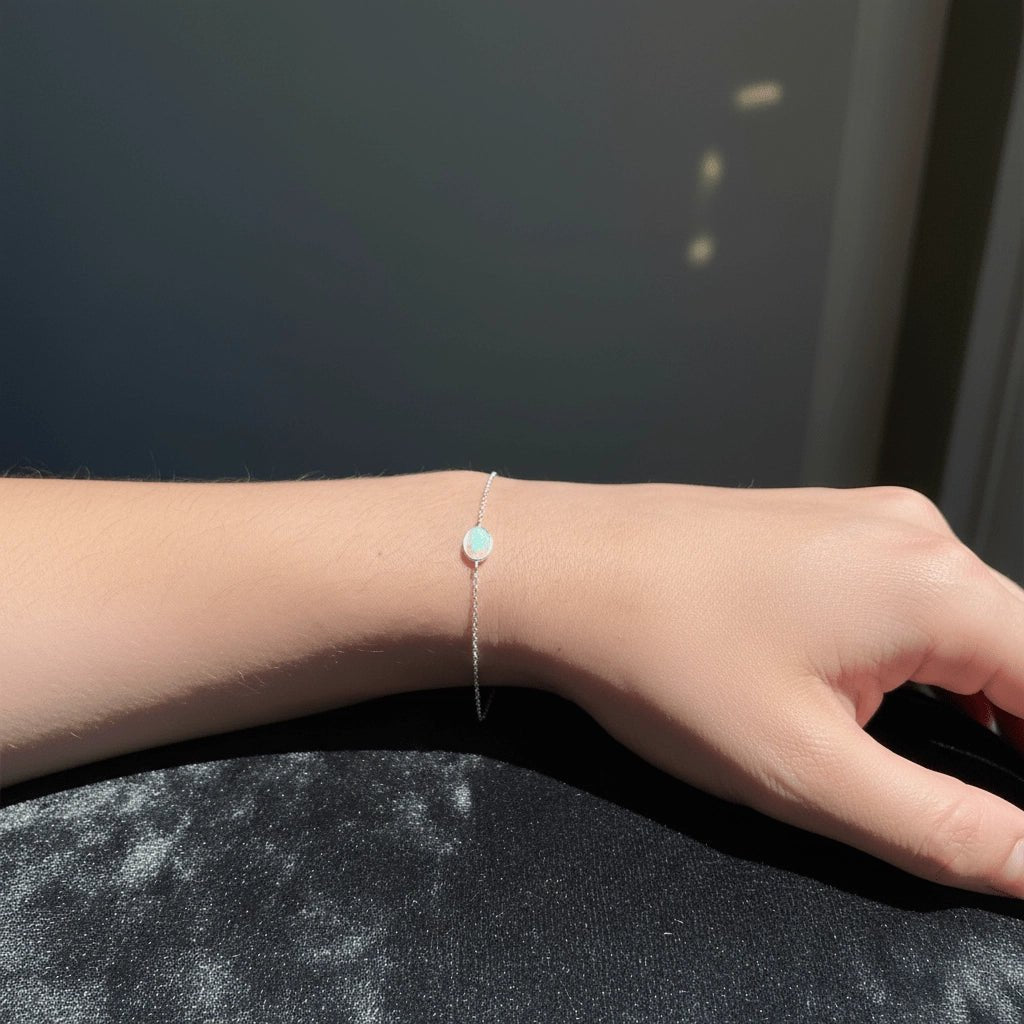 Hand wearing a delicate bracelet with a small round charm on a dark surface