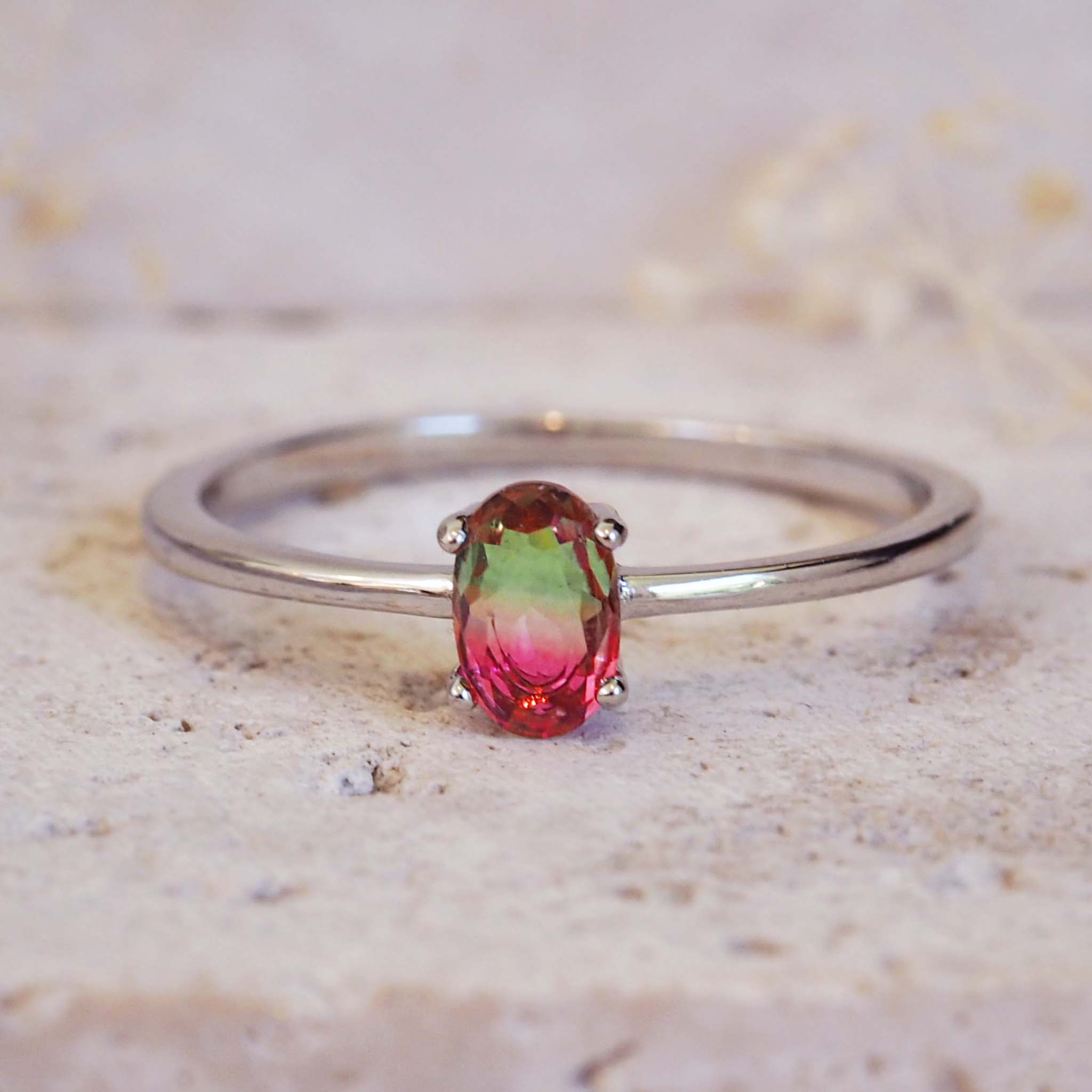 Silver ring with a multicolored gemstone on a textured beige background