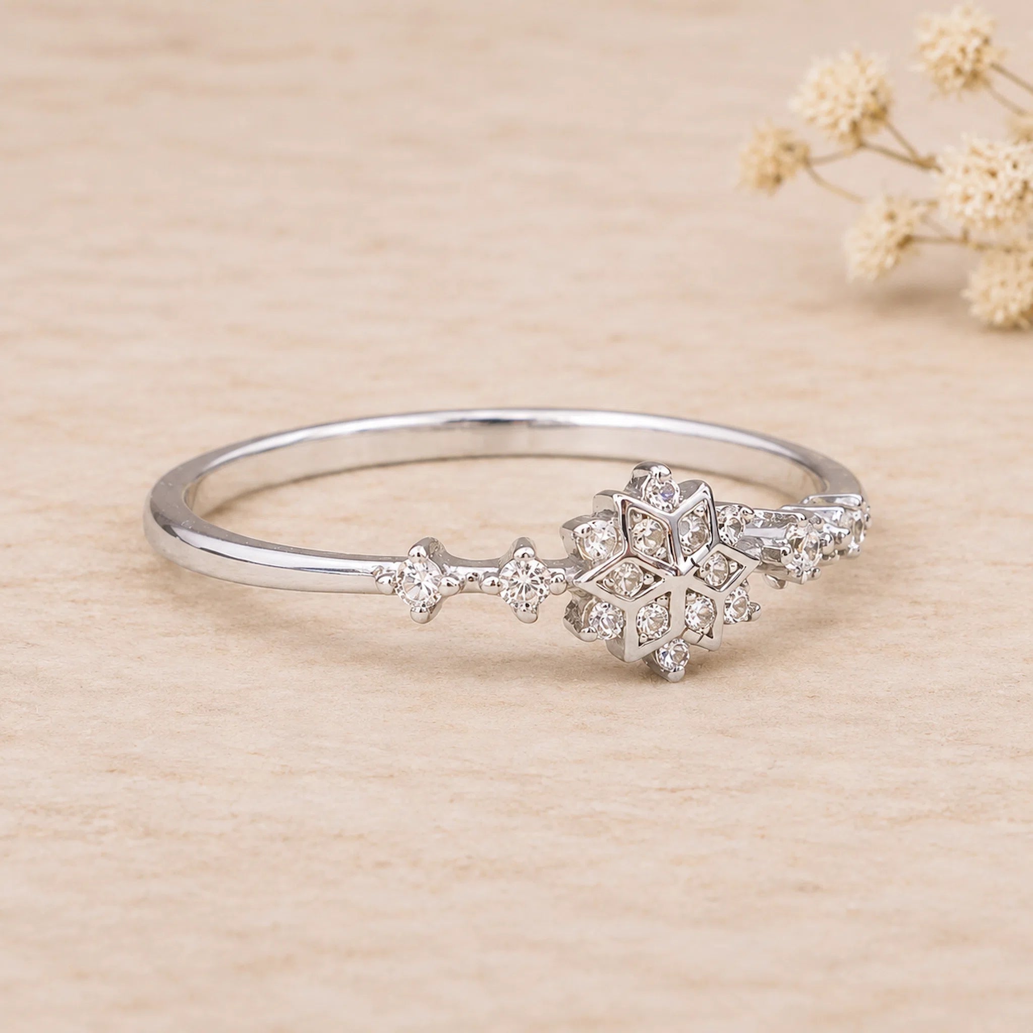 side view of a sterling silver ring with delicate snowflake design with cubic zirconias on a light background